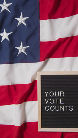 Vertical-Video-Of-Sign-Reading-Your-Vote-Counts-Lying-On-US-Stars-And-Stripes-Flag-For-American-Election-2024